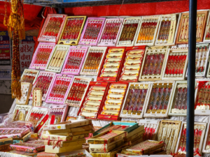 A colorful market stall displaying a wide variety of traditional Rakhi designs in red, pink, gold, and cream packaging, arranged across shelves and stacked boxes in Lucknow.