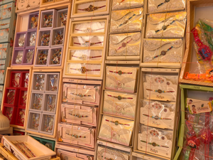 A colorful retail display featuring rows of intricately designed Rakhis arranged in decorative boxes and packaging, with traditional and floral patterns in pink, gold, red, and cream tones. The rakhi markets in Lucknow