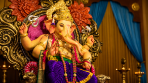 Lord Ganesha idol adorned with a golden crown, colorful garlands and traditional ornaments, seated on an ornate decorative throne with warm lighting, floral carvings, blue curtains and brass lamps in the background.