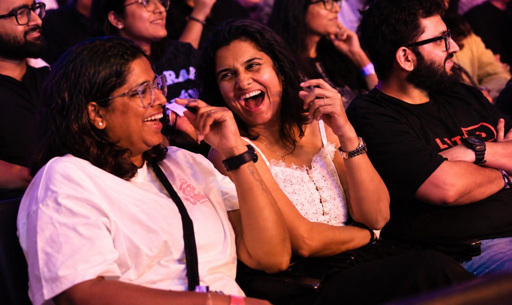 Audience members laughing and enjoying a live performance under vibrant red and purple stage lighting at Swati Sachdeva's show.