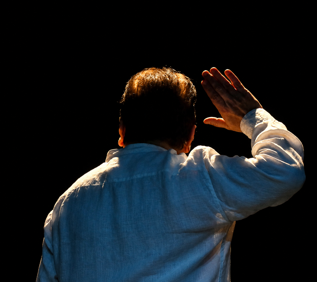 Roshan Abbas performing on stage with his hand raised against a dark background, from Indradhanush - A Pitara of Stories.