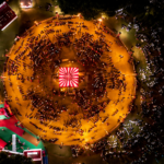 Aerial night view of Garba Nights in Lucknow, showing a large circular dance ground filled with people performing Garba around a brightly lit central stage, surrounded by colorful event areas and lights.