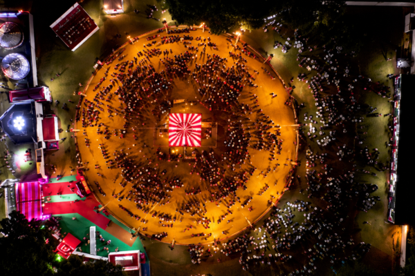 Aerial night view of Garba Nights in Lucknow, showing a large circular dance ground filled with people performing Garba around a brightly lit central stage, surrounded by colorful event areas and lights.