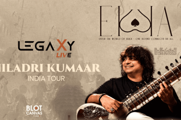 Promotional poster for Legaxy Live – Niladri Kumaar India Tour, featuring Indian classical musician Niladri Kumaar smiling while playing a sitar on the right side. The poster has a warm grey-beige textured background with subtle silhouettes of a live audience, musical elements, and architectural details. The left side prominently displays the “LEGAXY LIVE” logo, followed by the large text “NILADRI KUMAAR” and “INDIA TOUR.” The top right features the “EKKA” logo with the tagline “Enter the World of Ekka – One Sound Connects Us All,” while the bottom left includes “BLOT CANVAS.” The overall design has a vintage, artistic concert-poster aesthetic in muted grey, beige, black, cream, and brown tones.