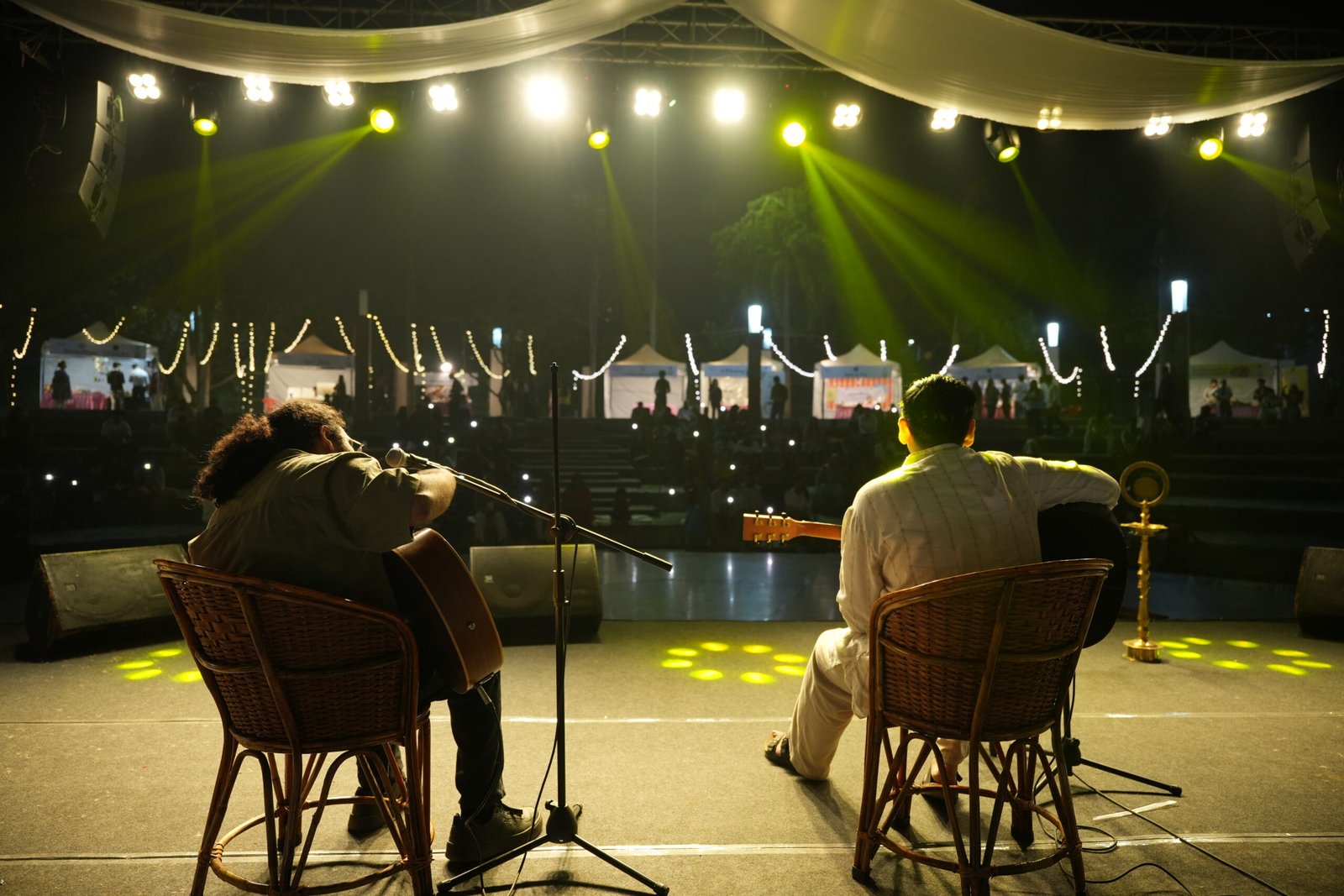 RJ Tashi and Kartik Mishra performing live at Spill The Word Fest Season 4, Day 1, on 24 October 2026, organised by Kavita Kisse Kahaniyan at Lohia Park, Lucknow, with guitars, vibrant stage lighting, and illuminated festival stalls in the background.